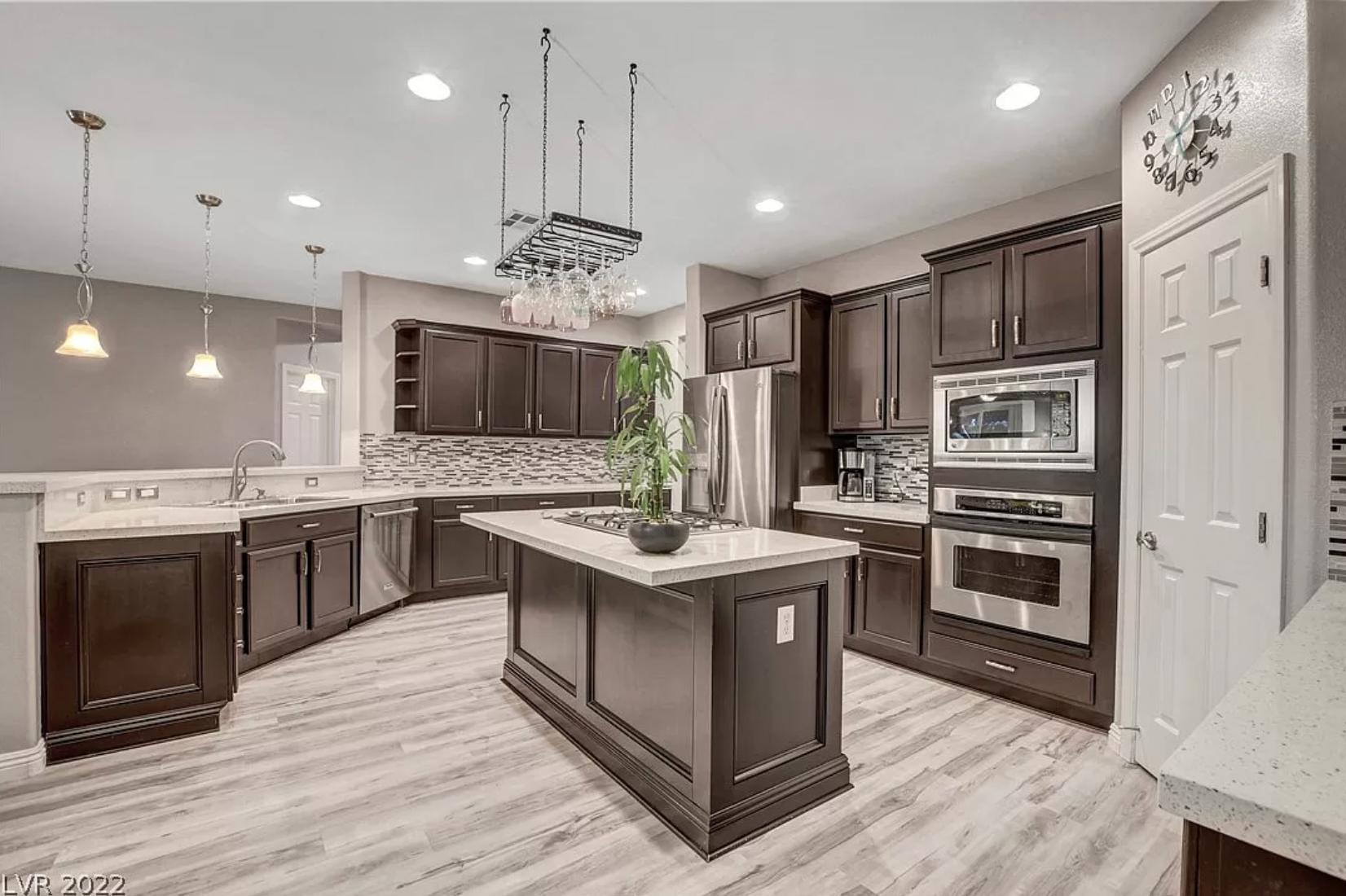 A modern kitchen in shades of gray with stainless steel appliances, dark cabinetry, and quartz countertops